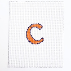 May include: A cross-stitch design of the letter "C" in orange with a dark purple outline, centered on a white canvas. The canvas has a grid-like texture, and the stitching is visible.