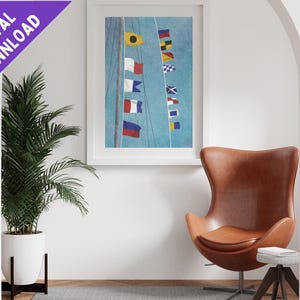 May include: A framed print of a nautical flag design with a blue background and a white mast. The flags are colourful and feature various designs. The print is hanging on a white wall in a room with a brown leather egg chair.