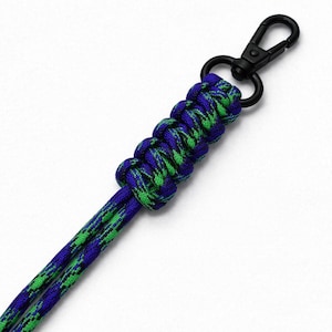 May include: A blue and green paracord lanyard with a black metal clasp. The lanyard is made of braided cord in a pattern of blue and green. The clasp is a swivel type.