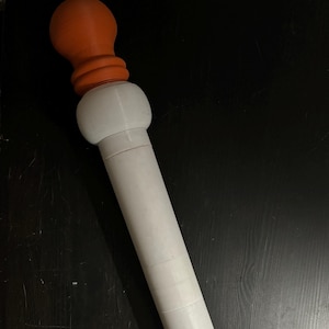 May include: A white rolling pin with orange end caps. The rolling pin is made of plastic and has a smooth surface.