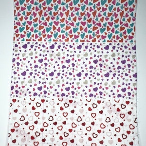 May include: Three fabric swatches with a white background and a repeating pattern of small red, pink, purple, and teal hearts.