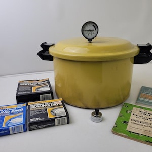 Puede incluir: Una olla a presión Presto amarilla con un asa negra y un indicador en la parte superior. También hay varias cajas de anillos de sellado Presto y manuales de instrucciones. La olla está diseñada para envasar y cocinar a presión.