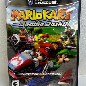 Könnte beinhalten: Eine Nintendo GameCube Videospielhülle für Mario Kart Double Dash!! mit Mario und Luigi in einem rot-blauen Kart auf dem Cover. Das Artwork zeigt verschiedene Charaktere, den Spieletitel und den Text Team Up for Twice the Fun!