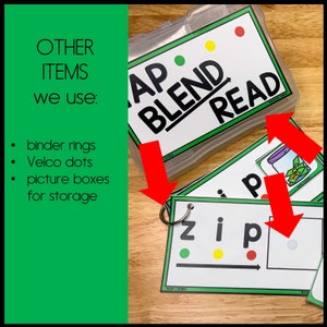 May include: A set of green and white flashcards with the words "AP BLEND READ" on one card and "zip" on another card. The cards are organized in a clear plastic container with red, yellow, and green dots on the front. The cards are used for teaching phonics and reading.