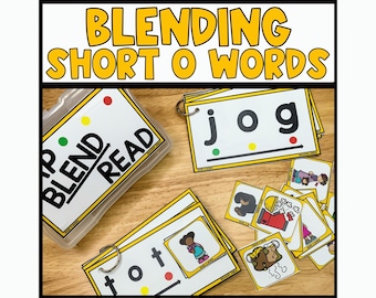 May include: A set of yellow and white flash cards with the words "Blend Read" on a clear plastic container. The cards have the words "jog", "tot", and other short vowel words. The cards also have pictures of a person jogging, a person wearing a hat, and other pictures.