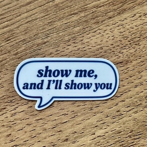 May include: A white speech bubble sticker with a dark blue border and the dark blue text "show me, and I'll show you" printed in the center. The sticker has a rounded rectangular shape with a small triangular tail pointing downward.