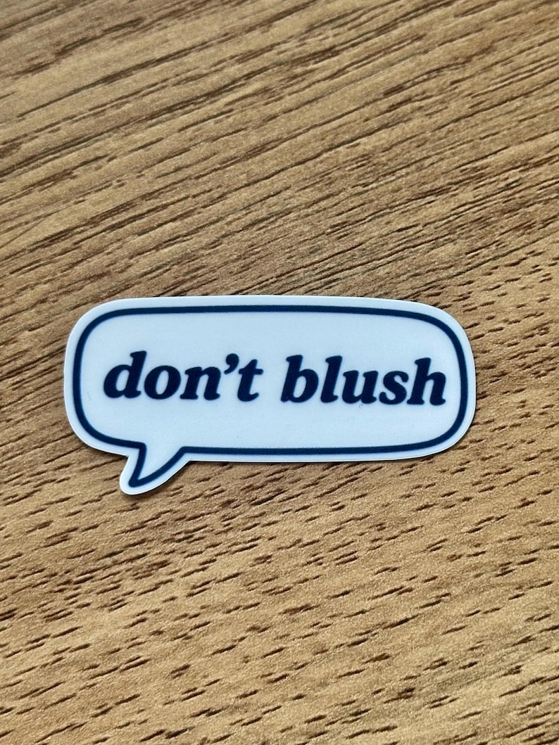May include: A white speech bubble sticker with a dark blue outline and the text "don't blush" printed in dark blue lowercase letters. The sticker has a rounded rectangular shape with a small tail pointing downwards on the left side.