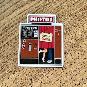 May include: A rectangular sticker depicting a vintage photo booth with a red curtain. The booth features the text "PHOTOS" at the top, "4 poses 3 minutes" on the side, and a sign hanging on the curtain that reads "OUT OF ORDER". Legs are visible.