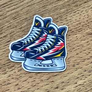 May include: A die-cut sticker featuring a pair of dark blue ice skates with white laces and a lightning bolt graphic in red and yellow on the side. The skates have silver blades and are outlined in white, presented as a single graphic illustration.