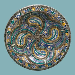 May include: A round, decorative plate with a detailed, colorful design. The plate features a silver filigree border and a central pattern of swirling blue, yellow, and teal shapes. The design is symmetrical and intricate, with small, dotted accents.