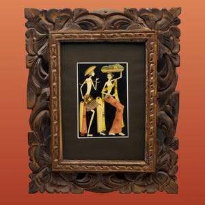 Könnte beinhalten: Ein gerahmtes Kunstwerk mit einem Gemälde von zwei Figuren in traditioneller Kleidung. Die Figuren sind in einem minimalistischen Stil mit gelben, orangefarbenen und schwarzen Akzenten dargestellt. Das Kunstwerk befindet sich in einem dunkelbraunen Rahmen mit kunstvollen, geschnitzten floralen Details.