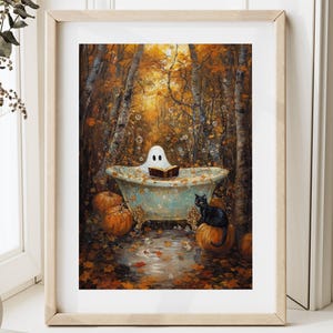Op de afbeelding: Een ingelijste prent toont een grillige Halloween-scène. Een witte geest leest in een vintage badkuip in een bosrijke omgeving. Een zwarte kat zit op een pompoen, met andere pompoenen eromheen. De achtergrond toont herfstbladeren.