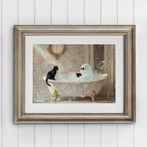 Op de afbeelding: Een ingelijste prent toont een zwarte kat en een spook in een vintage badkuip vol bellen. Het spook, gehuld in een wit laken, leest een boek. De kuip heeft gouden accenten en staat in een kamer met bloemenpatroon.
