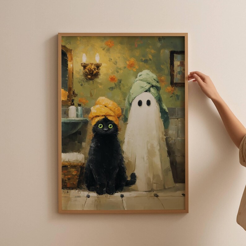 May include: A framed art print depicts a black cat wearing a yellow towel turban and a ghost wearing a green towel. The cat has green eyes. The background shows a bathroom with floral wallpaper and a mirror.