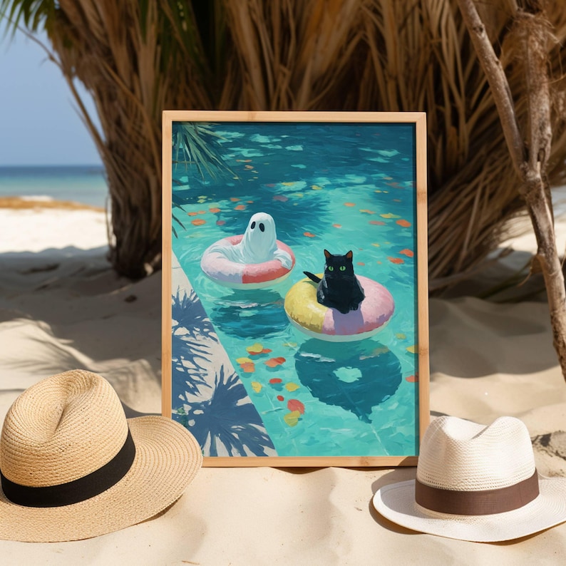 Op de afbeelding: Een ingelijste kunstdruk toont een geest en een zwarte kat op opblaasbare ringen in een turquoise zwembad. De afdruk zit in een houten frame. Twee strohoeden staan op de voorgrond.