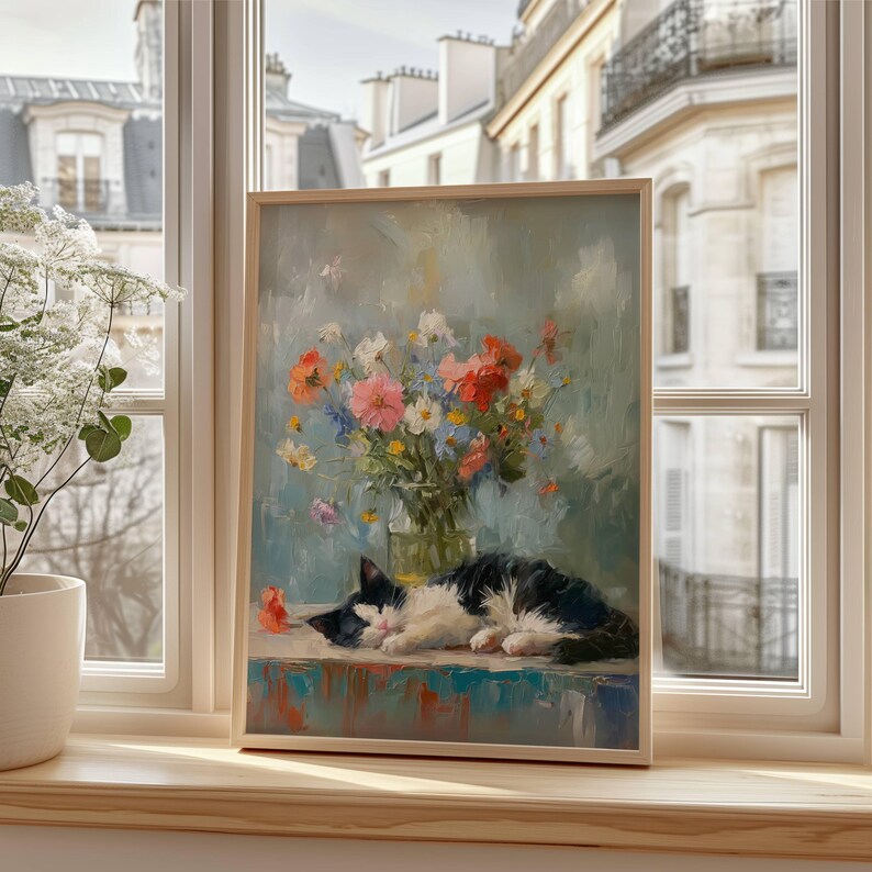 May include: A framed painting depicts a black and white cat sleeping on a table. A vase of colorful flowers sits behind the cat. The painting is set against a light blue background. The frame is made of light-colored wood.