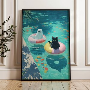 Op de afbeelding: Ingelijste kunstafdruk met een grillige sc&egrave;ne van een zwarte kat en een spook die in een zwembad op opblaasbare ringen drijven. Het zwembadwater is turquoise, met kleurrijke bladeren. Het kunstwerk is in een zwarte lijst.