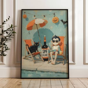 May include: A framed art print depicts a whimsical scene of a vampire lounging on a beach chair with a black cat, under an orange and white umbrella. A bottle of SPF 10,000 sunscreen is nearby, with Halloween decorations in the background.