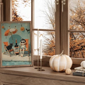 May include: A framed print depicts a cartoon scene of a vampire relaxing at a pool with a black cat, a bottle of SPF 10,000, and Halloween decorations. A white pumpkin, two smaller pumpkins, and books sit on a wooden surface near a window.