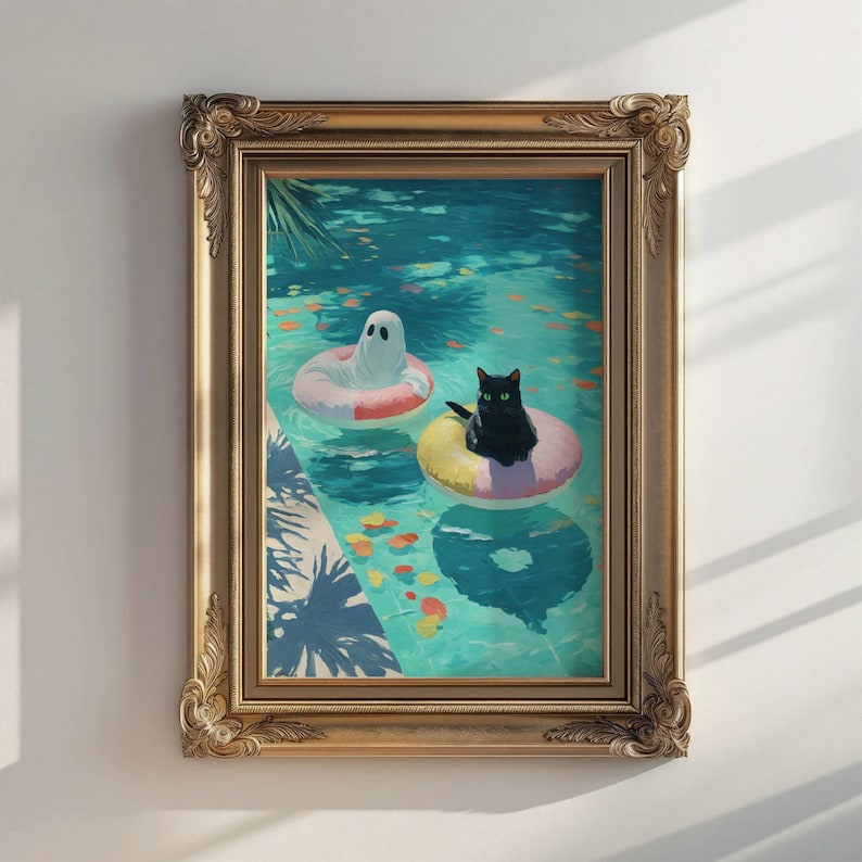 Op de afbeelding: Een ingelijste kunstdruk toont een spook en een zwarte kat die in een zwembad op opblaasbare ringen drijven. Het zwembadwater is turquoise, met kleurrijke bladeren. Het kunstwerk is ingelijst in een gouden, sierlijke lijst.