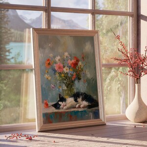 May include: A framed painting of a black and white cat resting on a table, with a vase of colorful flowers. The painting is set in front of a window with a view of mountains and a lake. A vase with red branches sits nearby.