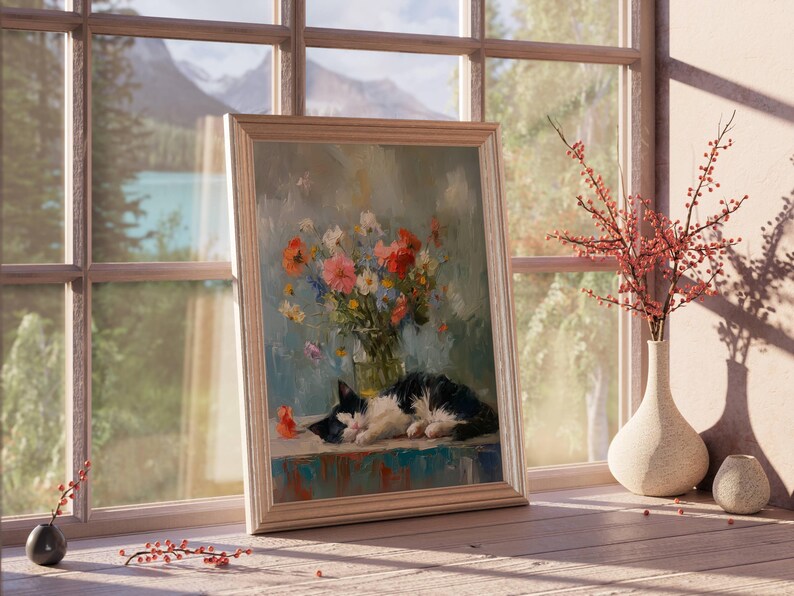 May include: A framed painting of a black and white cat resting on a table, with a vase of colorful flowers. The painting is set in front of a window with a view of mountains and a lake. A vase with red branches sits nearby.