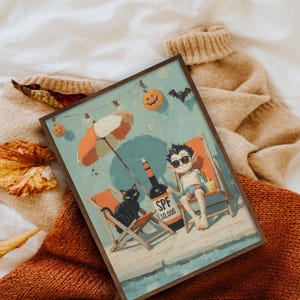 May include: A framed art print depicts a vampire relaxing on a beach chair with a black cat, under an orange and white umbrella. A bottle of SPF 10,000 sunscreen sits nearby. The scene is set against a blue sky with Halloween decorations.