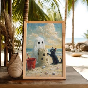 Puede incluir: Una impresi&oacute;n art&iacute;stica enmarcada representa una escena de playa caprichosa. Una figura de fantasma y un gato negro construyen un castillo de arena junto a un cubo rojo. La obra de arte est&aacute; ambientada en una playa arenosa con conchas marinas, bajo un cielo nublado. El marco es de madera clara.