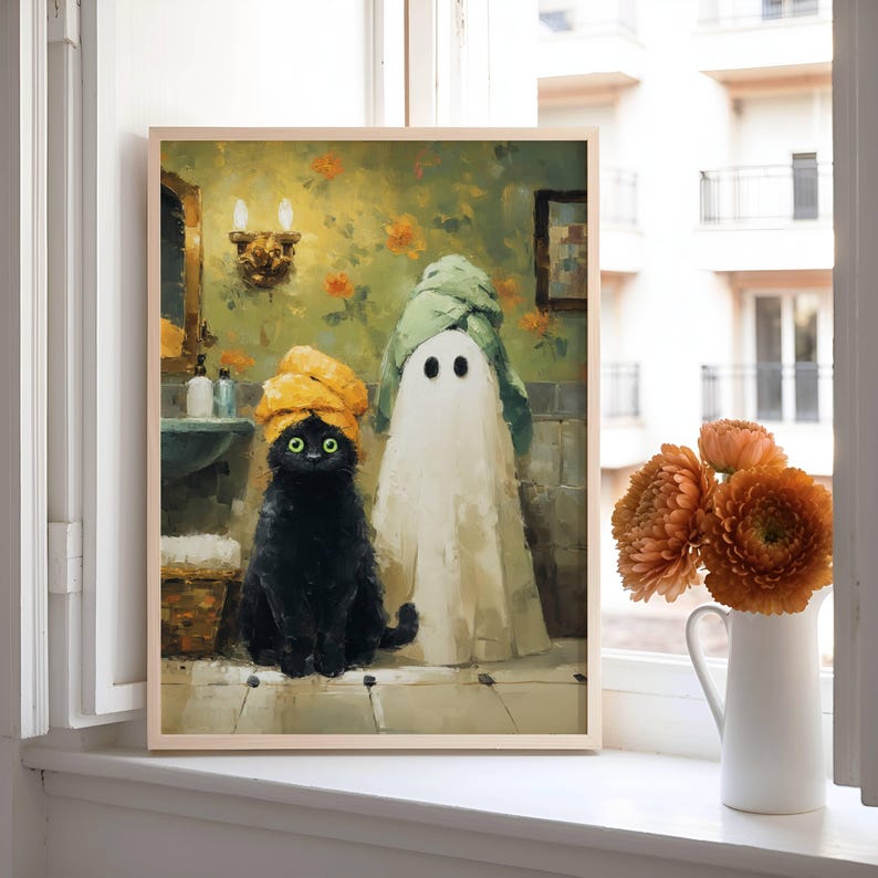 May include: A framed art print featuring a black cat and a ghost, both wearing towels, in a bathroom setting. The cat has green eyes and a yellow towel. The ghost is draped in a white sheet and a green towel. The background has floral wallpaper.