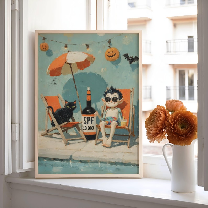 May include: A framed print depicts a whimsical scene of a vampire and a black cat relaxing on beach chairs under an orange and white umbrella. A bottle of SPF 10,000 sunscreen sits nearby. Halloween decorations, including jack-o'-lanterns and a bat, are in the background.