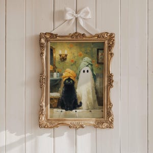 May include: A framed painting depicts a black cat and a ghost in a bathroom setting. The cat wears a yellow towel turban, and the ghost is draped in a white sheet. The ornate gold frame is suspended by a white ribbon.