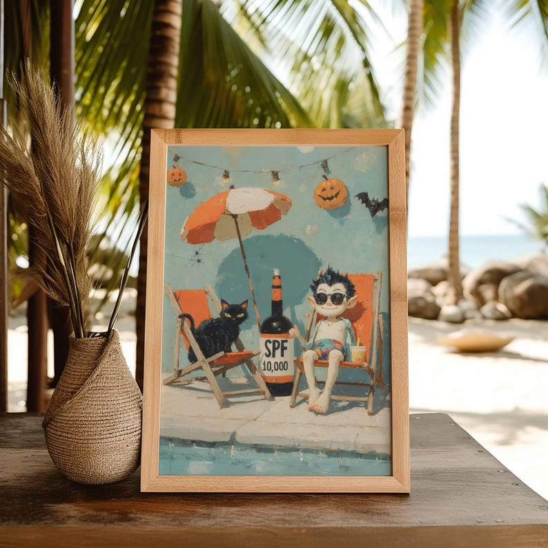 May include: A framed print featuring a whimsical illustration of a vampire and a black cat relaxing on beach chairs under an orange and white umbrella. A bottle of SPF 10,000 sunscreen is placed between them. Halloween-themed decorations are in the background.