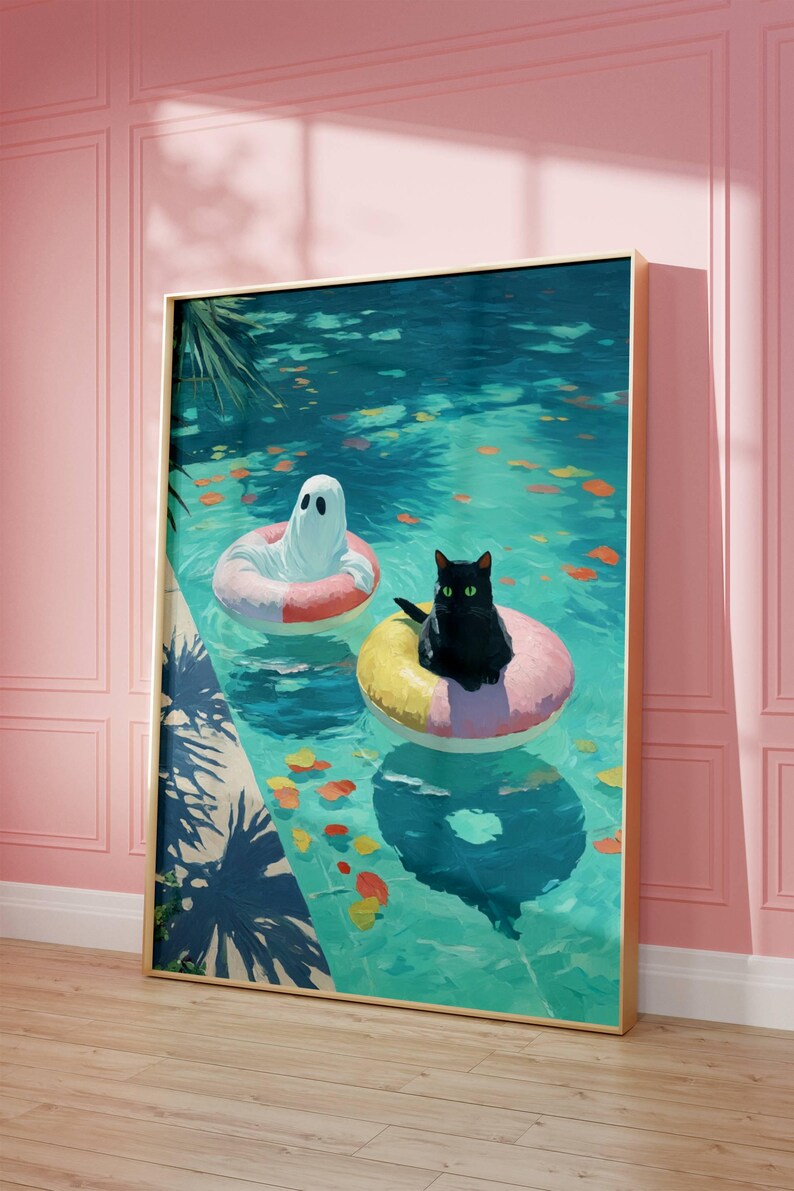 Op de afbeelding: Een ingelijste kunstdruk toont een geest en een zwarte kat die in een zwembad op opblaasbare ringen drijven. Het zwembadwater is turquoise, met kleurrijke bladeren. Het kunstwerk is ingelijst in goud.
