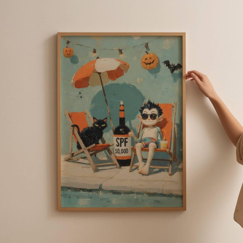 May include: A framed print depicts a whimsical beach scene with a vampire, black cat, and bottle of SPF 10,000. The vampire is in sunglasses, sitting in a beach chair under an orange and white umbrella. Pumpkins and a bat decorate the background.