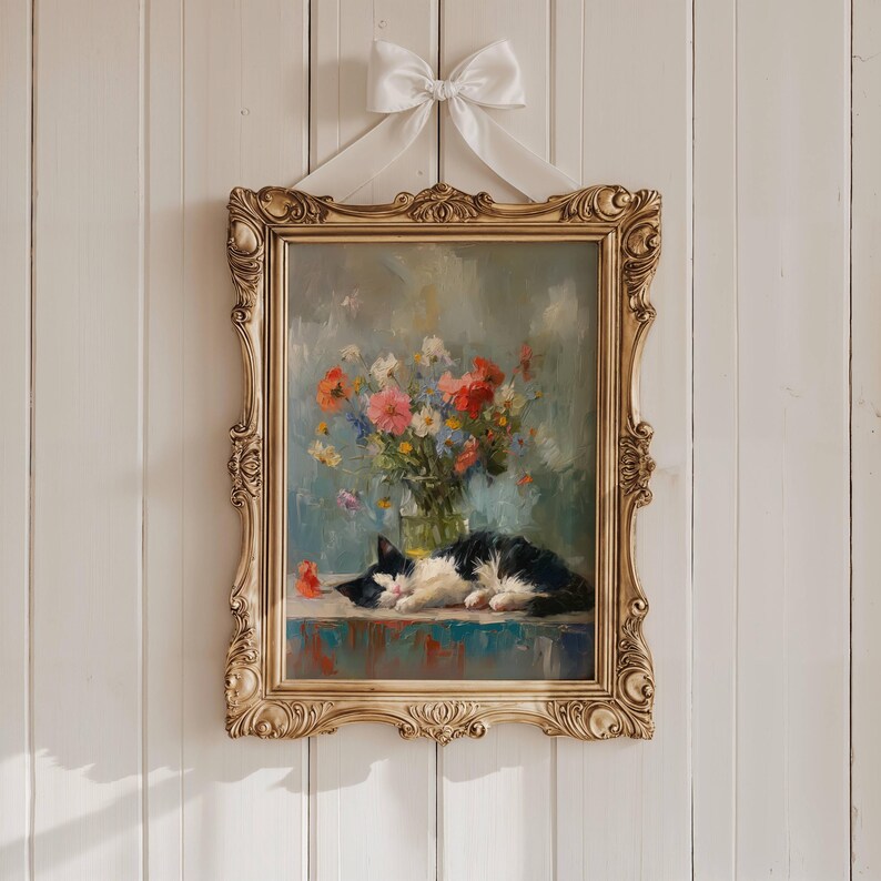 May include: Ornate gold framed painting of a black and white cat resting on a table, with a vase of colorful flowers. The painting is hung with a white ribbon and bow. The artwork has a vintage aesthetic.