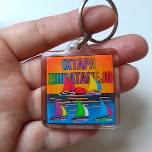 May include: A clear plastic keychain with a metal ring. The keychain features a colorful graphic of sailboats on the water with the text "IXTAPA ZIHUATANEJO". The sailboats have red, yellow, blue, and green sails.