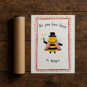 May include: A charming illustration on white paper with a red border. The image shows a cartoon bee in a top hat and cape, holding a wand. Text reads, "Do you bee-lieve in magic." A brown poster tube is on the left.