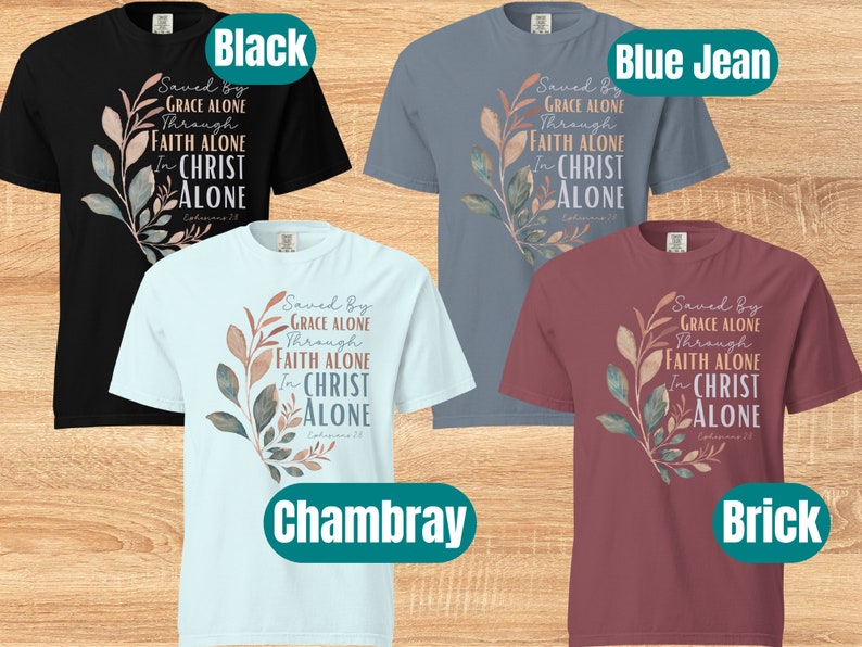 May include: Four t-shirts in different colours: black, blue jean, chambray, and brick. Each shirt features a watercolour-style floral design with the text "Saved By Grace Alone Through Faith Alone In Christ Alone Ephesians 2:8".