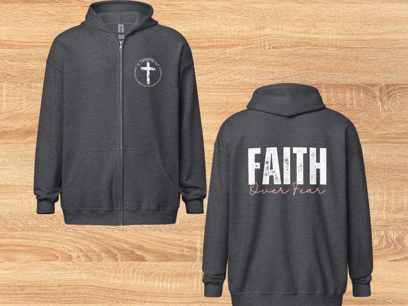 Puede incluir: Dos sudaderas con capucha de color gris oscuro con cremallera. Una sudadera tiene una cruz blanca con el texto "2 Timoteo 1:7" en un c&iacute;rculo en el pecho izquierdo. La otra sudadera tiene el texto "FAITH over FEAR" en blanco con letras rosas en la espalda.