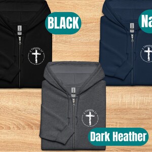Puede incluir: Tres sudaderas con capucha y cremallera en negro, azul marino y gris oscuro jaspeado con una cruz blanca y el texto "2 Timoteo 1:7" impreso en la parte delantera.