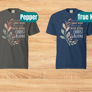 May include: Two t-shirts with a floral design and the text "Saved by Grace Alone Through Faith Alone In Christ Alone Ephesians 2:8". The t-shirts are in the colours pepper and true navy.