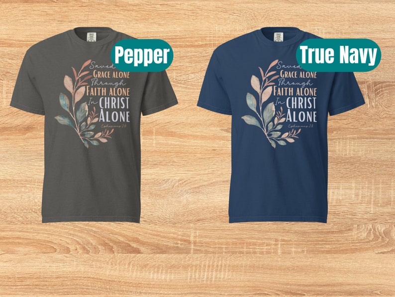 May include: Two t-shirts with a floral design and the text "Saved by Grace Alone Through Faith Alone In Christ Alone Ephesians 2:8". The t-shirts are in the colours pepper and true navy.