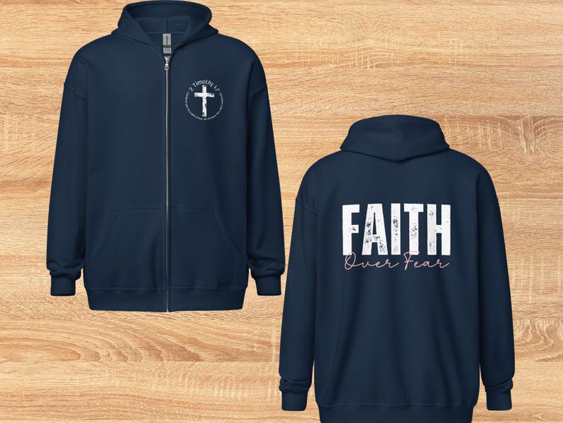 Puede incluir: Dos sudaderas con capucha azul marino con cremallera. La sudadera delantera tiene una cruz blanca con el texto "2 Timoteo 1:7" en un c&iacute;rculo. La sudadera trasera tiene el texto "FAITH over FEAR" en blanco con letras rosas.