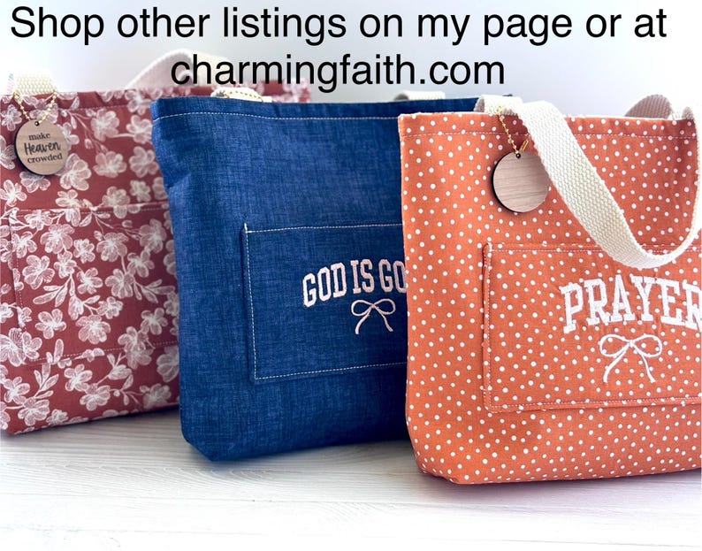 May include: Three tote bags in a row. The first is red with white floral patterns, the second is blue with "GOD IS GOOD" embroidered on the pocket, and the third is orange with white polka dots and "PRAYER" embroidered on the pocket. Each has a wooden tag.