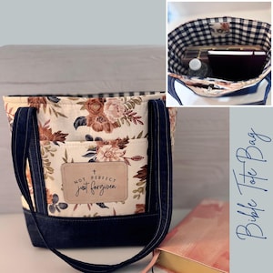 Op de afbeelding: Tote bag met bloemenprint en marineblauwe denim details. De tas heeft een crèmekleurige achtergrond met een bloemenpatroon in bruin en roze. De tekst "Not Perfect Just Forgiven" staat op een leren patch. De binnenkant heeft een ruitpatroon.