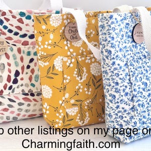 May include: Three fabric tote bags with white handles and exterior pockets. The bags feature different floral patterns in cream, yellow, and blue. Each bag has a wooden charm with inspirational text. The text "PRAY TRUST", "I am Child of God", and "Jesus over you" are visible.