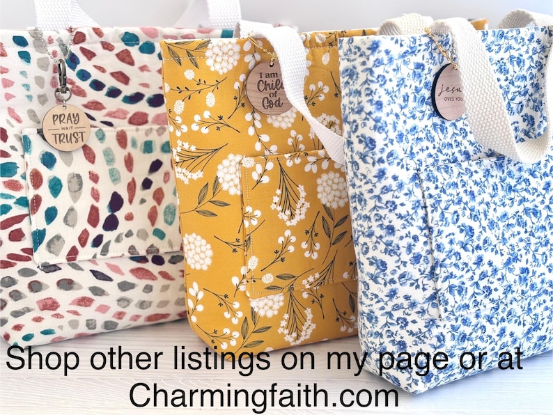 May include: Three fabric tote bags with white handles and exterior pockets. The bags feature different floral patterns in cream, yellow, and blue. Each bag has a wooden charm with inspirational text. The text "PRAY TRUST", "I am Child of God", and "Jesus over you" are visible.
