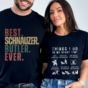 May include: A couple wearing black t-shirts with a Schnauzer theme. The man's shirt says "Best. Schnauzer. Butler. Ever." The woman's shirt says "Things I do in my spare time" and lists activities like "Love Schnauzer", "Show off my Schnauzer", and "Take photos of Schnauzer".