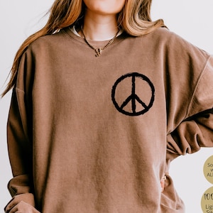 May include: Espresso-colored sweatshirt with a black peace sign graphic on the chest. The sweatshirt is made of 100% cotton and is lightweight. The text on the image says "Softness & warmth ALL season" and "Lightweight Sweatshirt".