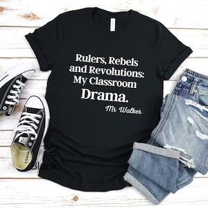 Peut inclure: T-shirt noir avec du texte blanc qui dit "Rulers, Rebels and Revolutions: My Classroom Drama. Mr. Walker"